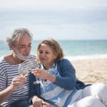 Pasangan lansia duduk bersama di pantai sambil menikmati suasana hari tua dengan tenang dan penuh kebersamaan.