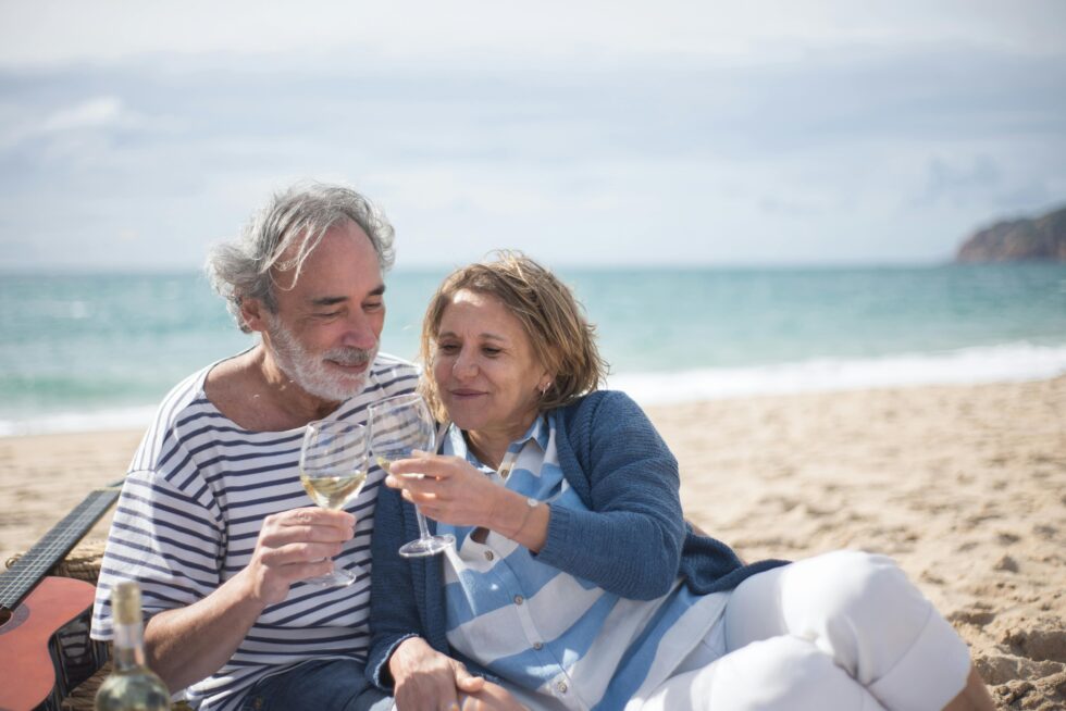 Pasangan lansia duduk bersama di pantai sambil menikmati suasana hari tua dengan tenang dan penuh kebersamaan.