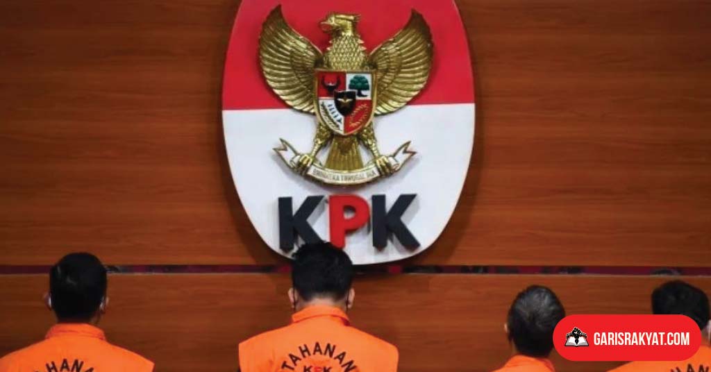 Logo KPK terlihat di latar belakang, dengan tersangka berdiri menghadap ke belakang.